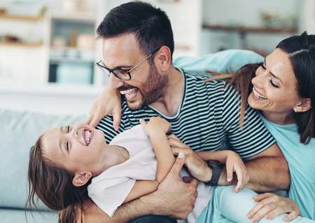Stock photo of two parents playing with a little girl at home.