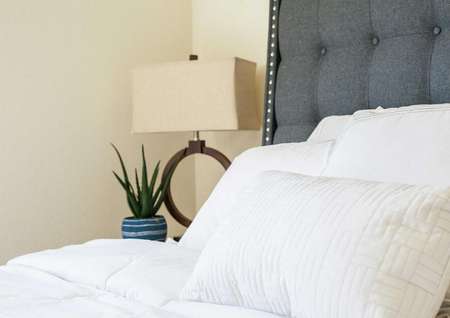 Driftwood home staged with bedroom furniture including bed with white sheets, grey headboard, and modern lamp
