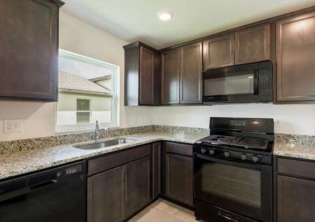 The Anastasia floor plans kitchen with tile floors, dark wood cabinets, a gas stove range and all black appliances.