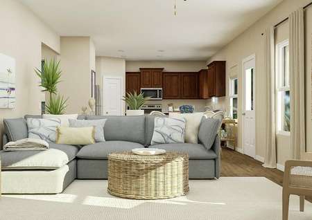 Rendering of the
  living room with two windows, tan walls and wood look flooring covered by a
  light-colored rug. Decorated with a large sectional couch and round wicker
  coffee table.