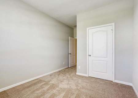 A bedroom in the Patricio model home with tan carpet, white baseboards and light tan walls