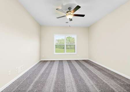 Photo of the primary bedroom overlooking the back yard with carpeting and a ceiling fan.