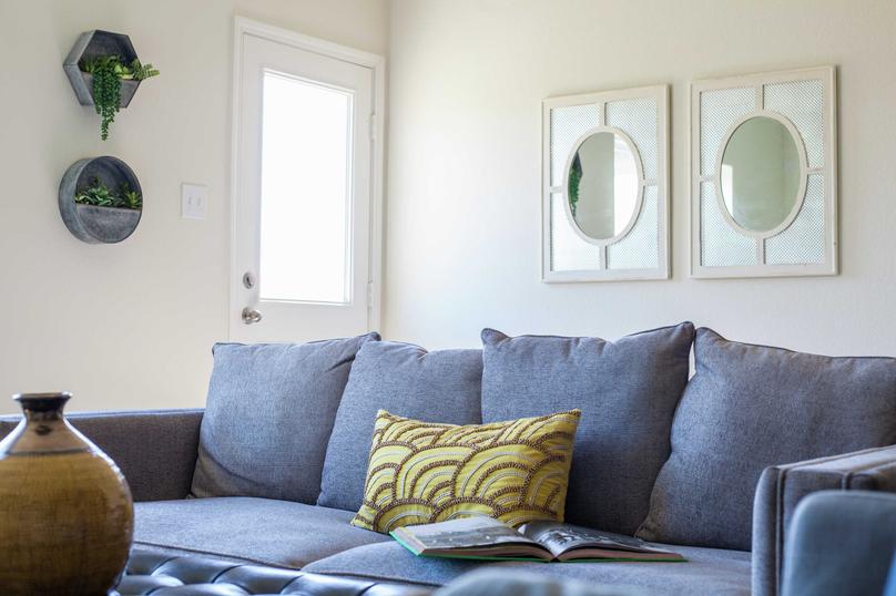 Model home staged with blue sofa with brown pattern throw pillow, mirror mounted on the wall, and decorative plants on the other wall