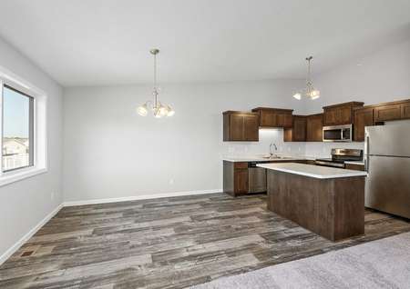 Interior photo of dinette and kitchen with island, brown cabinets and stainless appliances.