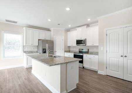 Kitchen with white cabinets with hardware, a large granite island and vinyl flooring.
