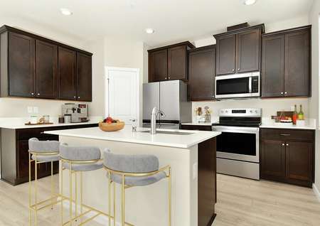 Open kitchen with an island and dark brown cabinets, three barstools and decor on quartz countertops.