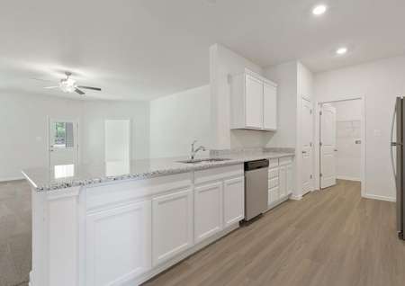 Spacious kitchen with sprawling granite breakfast bar overlooking family room with ceiling fan and door to backyard patio, white cabinets, plank flooring, recessed lighting, stainless dishwasher, pantry and laundry room.