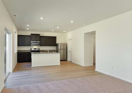 Open concept living, dining, kitchen with carpet and plank flooring, dark cabinetry in kitchen.