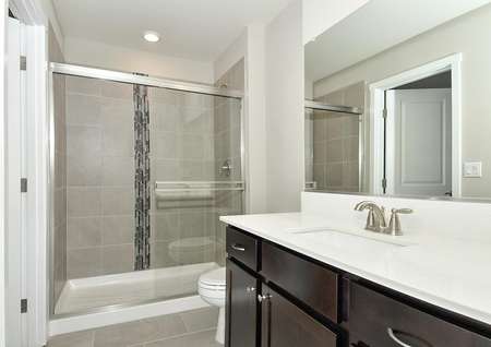 Bathroom with dark brown cabinets, spacious quartz countertop, shower/tub  combo with glass door and decorative wall tile.
