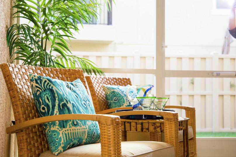 This home is complete with wooden chairs that have turquoise pattern pillows and beige cushions, table with glasses sitting on it, and a house plants in the background.