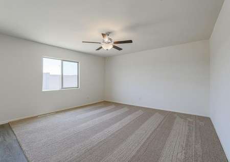 Spacious family room with tan carpet, ceiling fan and windows.