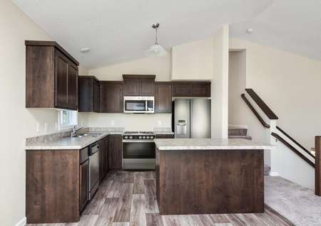 Photo of an open kitchen with island, brown cabinets with crown molding, plank flooring and stainless steel appliances.