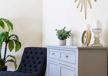 Staged model with a clock on a desk, plants and a dark blue chair. 