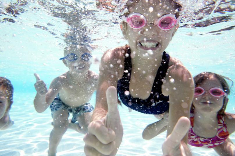 Children smiling underwater in a swimming pool at the Estrella community