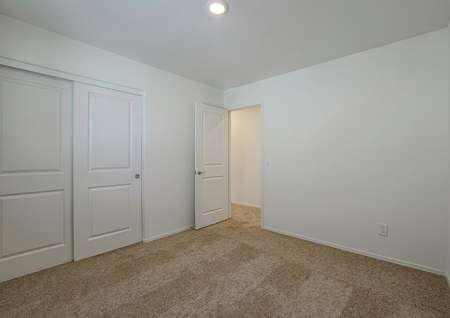 Guest bedroom with tan carpet and a closet with sliding doors.