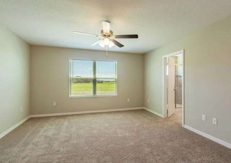 The Sorrento floor plans master bedroom that has a large window that is covered by blinds, carpet floors and tan walls.