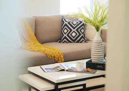 Staged home with sofa and navy pillow, yellow throw, coffee table and vase.