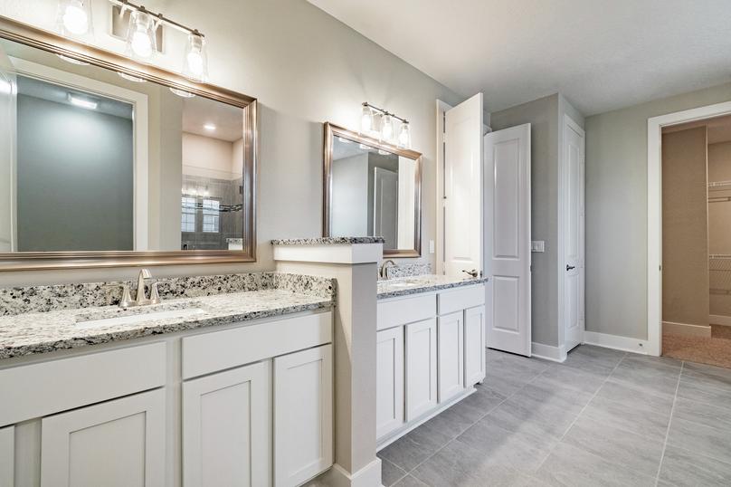 Master bathroom with split vanity, granite countertops, white cabinetry, two framed mirrors and tile flooring.