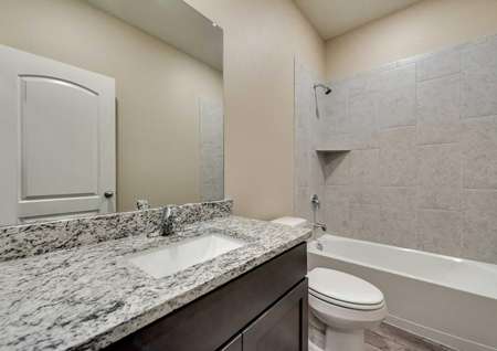 St. Clair guest bathroom with custom tile work, thick granite vanity, and brown cabinet