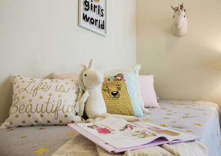 Staged children's room with open book, stuffed animals and throw pillows on the bed.