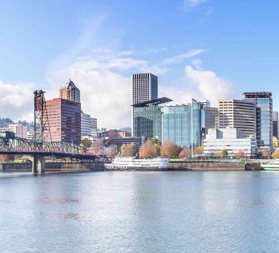 Portland, Oregon cityscape showing calm waters, railbridge, and numerous skyscrapers in the distance