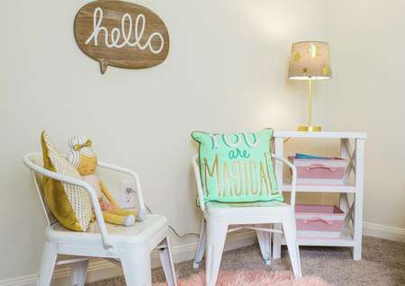 Kid's playroom with wooden sign on the wall, two kid's chairs with pillows and a shelf with lit lamp in the corner.