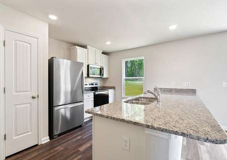 Angled image of the chef-ready kitchen with granite countertops, stainless steel appliances, recessed lighting, white cabinetry with hardware and an undermount kitchen sink. 