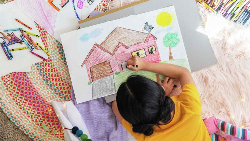 Girl coloring photo of home on rug.
