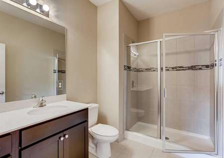 The Mateo model home's master bathroom with dark brown cabinets, tile flooring, a walk-in shower and cultured marble countertops
