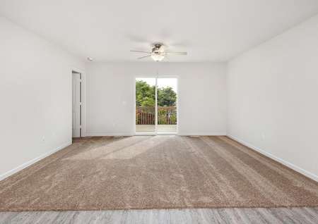 Photo of spacious living room with carpet, a ceiling fan, and sliding glass door to back yard.
