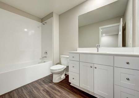 The secondary bathroom in the Kennedy floor plan with a bathtub/shower combo, vinyl wood floors and marble countertops.