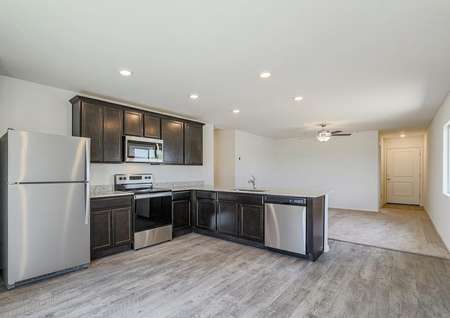 Open kitchen with stainless steel appliances and dark cabinets.