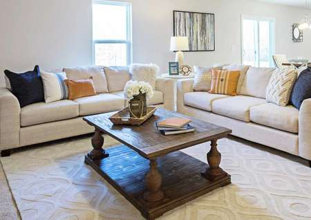 Living room with a white sofa and loveseat, brown wooden coffee table, and large light colored throw rug.