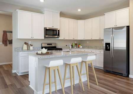 Staged kitchen with white cabinetry, stainless steel appliances and white bar stools.