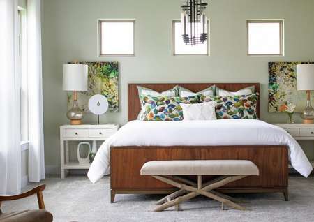 Staged bedroom with bed that has a white comforter, nightstand, and curtains. 