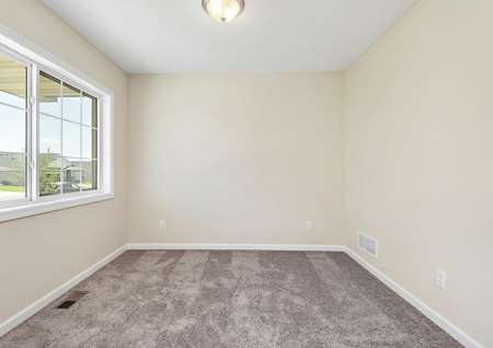 Photo of a carpeted flex room off the foyer with a wide window looking out at the front porch.
