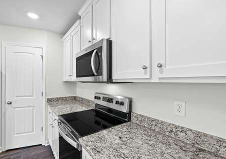 Kitchen with stainless steel appliances, granite countertops and white cabinets with hardware.