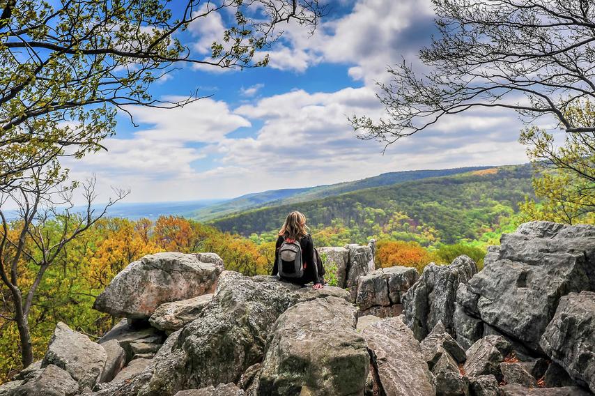 Maryland Appalachian Mountains during Autumn showing woman sitting on rocky outcropping, trees that have lost their leaves, and rolling hills of vegetation