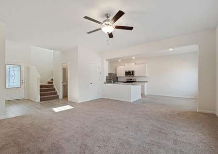 Spacious family room with carpet and ceiling fan opens to the dining room and kitchen to the right and a foyer to the left, with stairs leading to second floor.