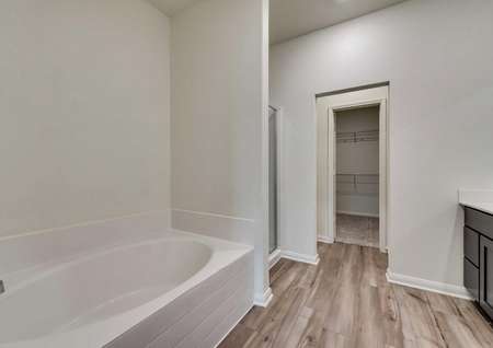 Master bathroom in the Oakmont floor plan with light vinyl flooring and large tub with separate shower with glass door and walk in closet
