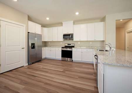 The spacious kitchen has white cabinetry, granite countertops, wood style flooring and more.