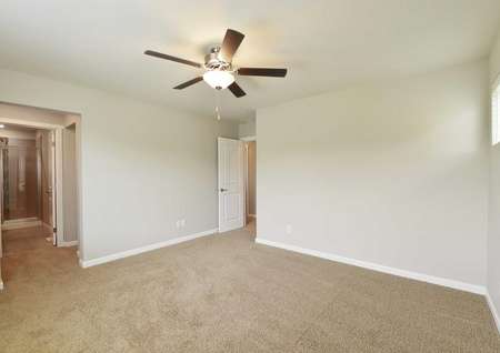 The Northwest Cypress master bedroom is shown with brown carpet and ceiling fan with master bathroom entrance.
