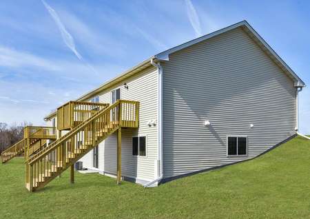 Photo of the backyard of a split-level home with a walkout basement and upstairs wooden deck with stairs to backyard.