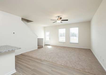 Spacious living room with carpet, ceiling fan and two windows near entry with glass front door.