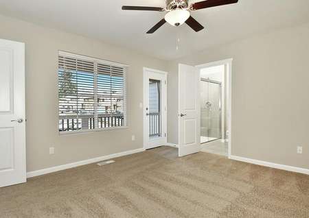 Photo of master bedroom with ceiling fan, carpet, double window with blinds, glass door leading to balcony and adjacent bathroom.