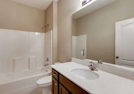 Secondary bathroom in the Santa Maria model home. White shower and tub combo, cultured marble countertops and dark brown cabinets