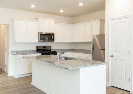 Close up of kitchen with white cabinets, granite counters, stainless refrigerator, gas range and microwave.