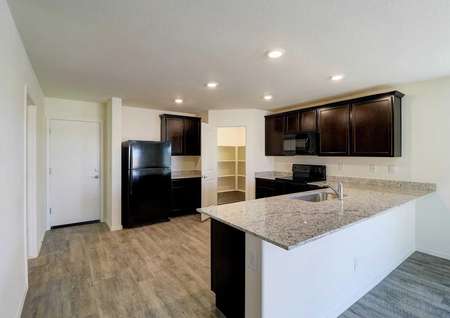 The kitchen with a pantry, brown wooden cabinets, granite countertops and black appliances in the Guadalupe floor plan.