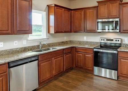 Recessed lighting, crown molding on light brown cabinets, granite countertops, vinyl wood-style flooring, and stainless steel appliances in the Hartwell model