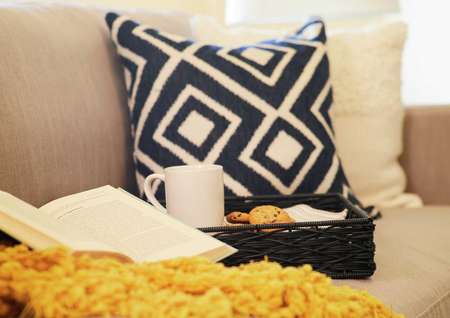 Staged home with light color couch, black and white patterned pillow and an open book. 